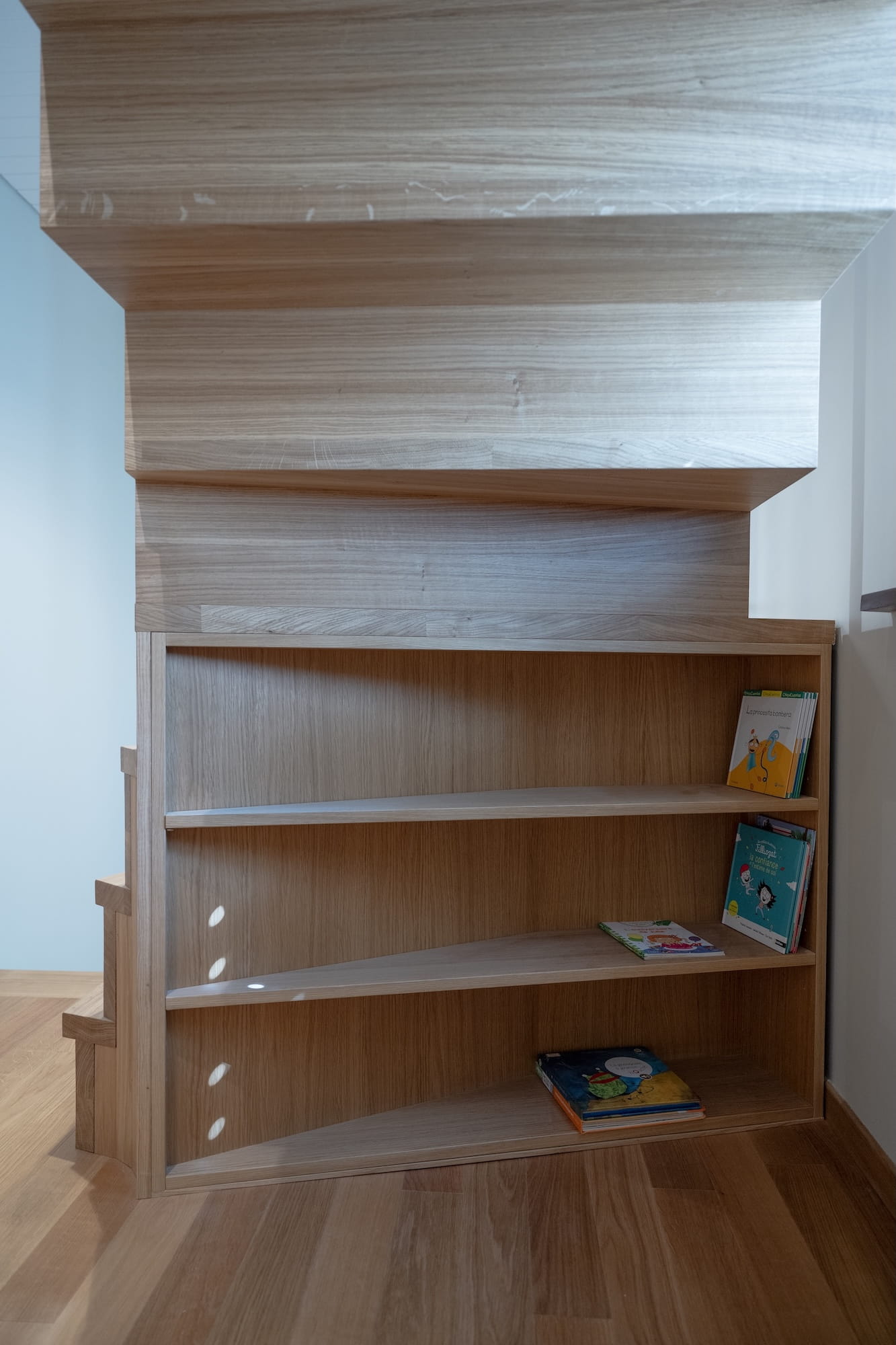 bibliothèque secondaire cheminée Petite bibliothèque en bois intégrée sur-mesure sous les marches d'un escalier étroit.